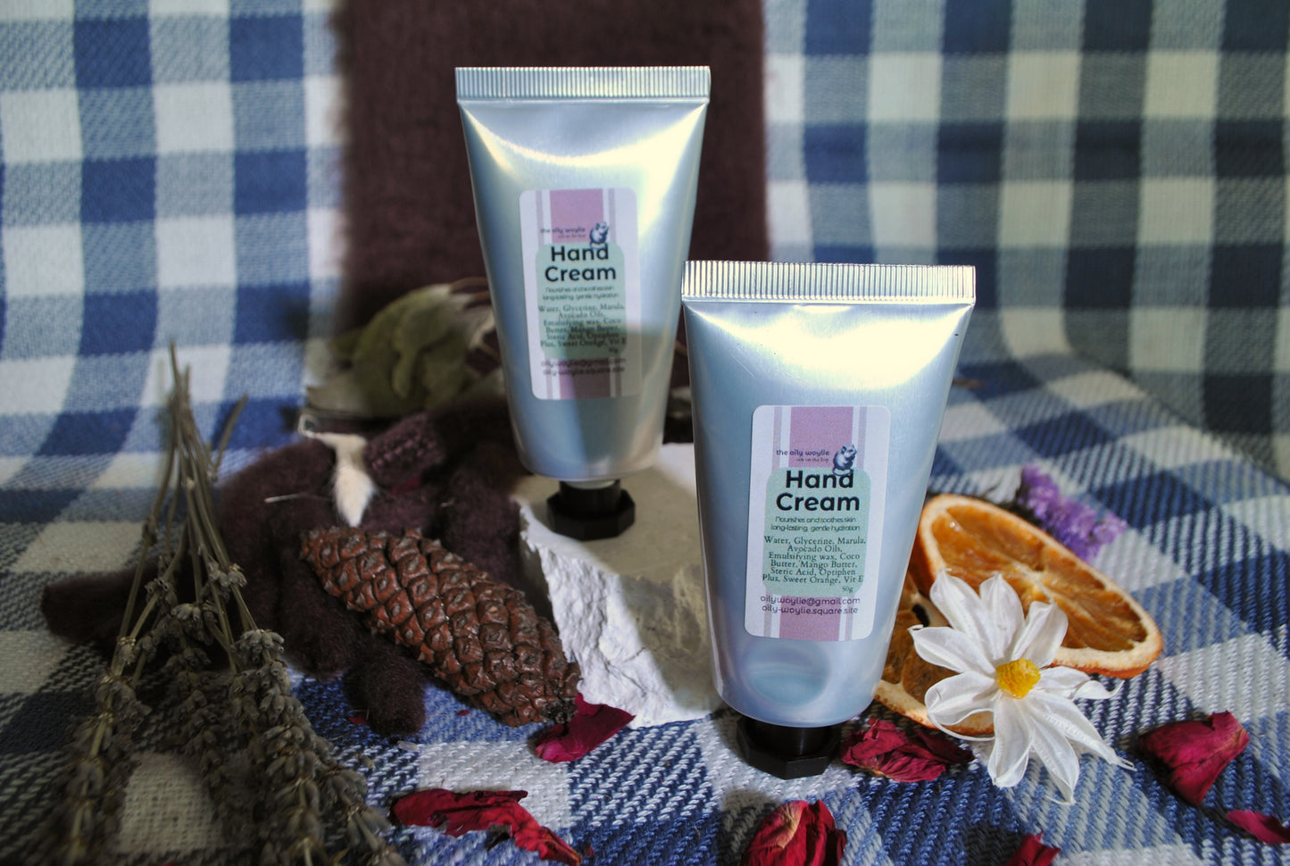 Two tubes of hand cream on a checkered fabric background with dried oranges and flowers.