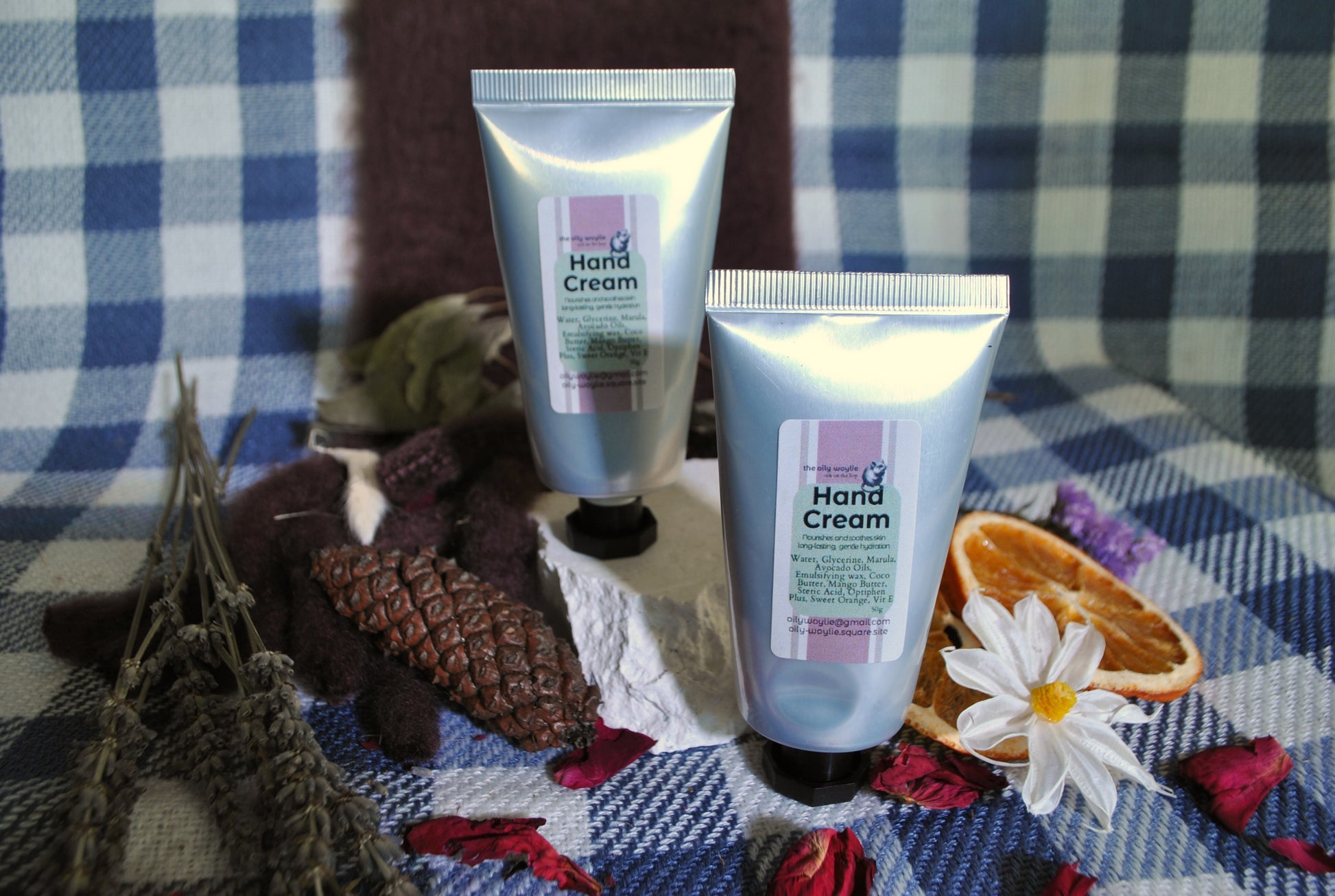 Two tubes of hand cream on a checkered fabric background with dried oranges and flowers.
