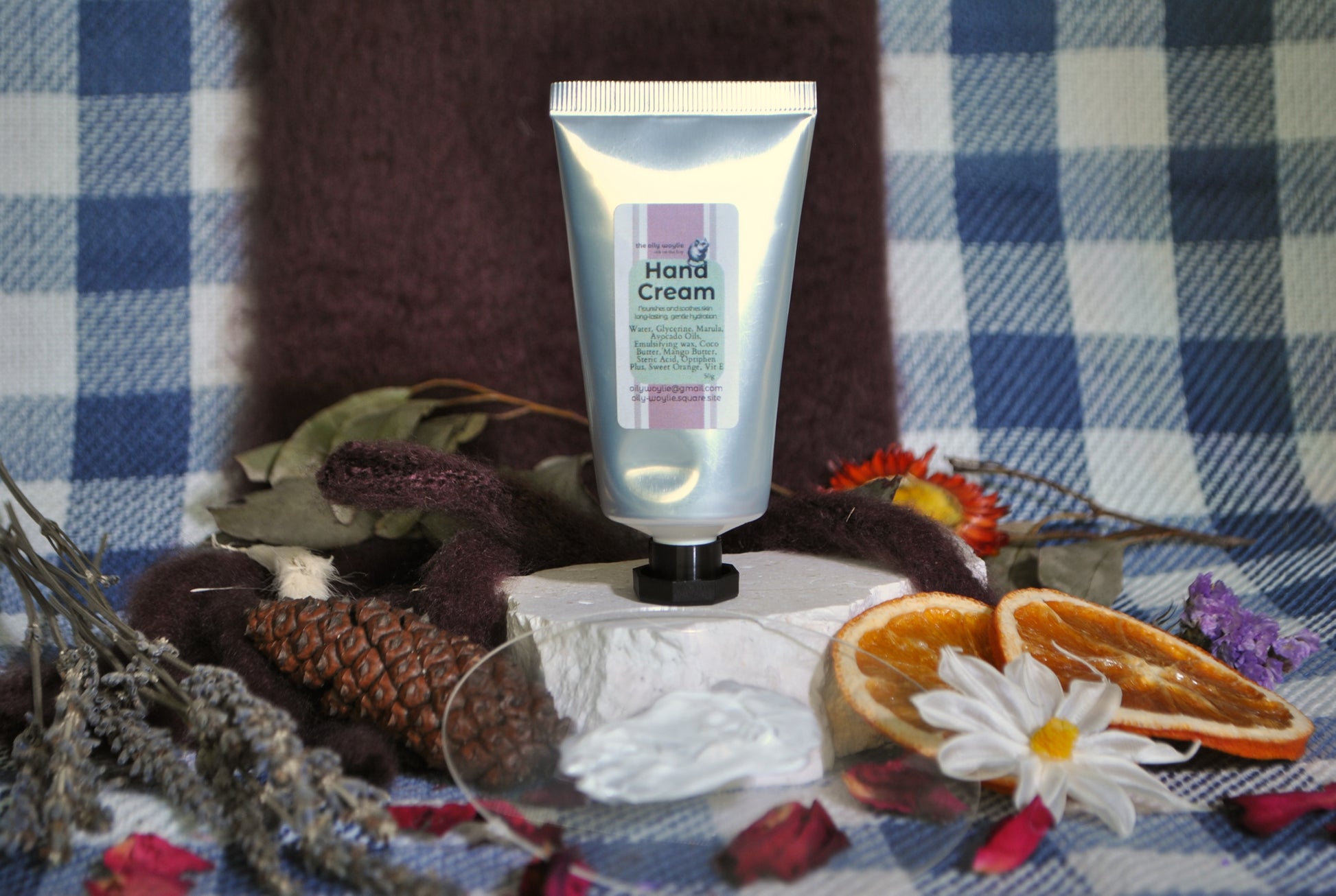 Hand cream on a stand with dried flowers and oranges on a checkered fabric background