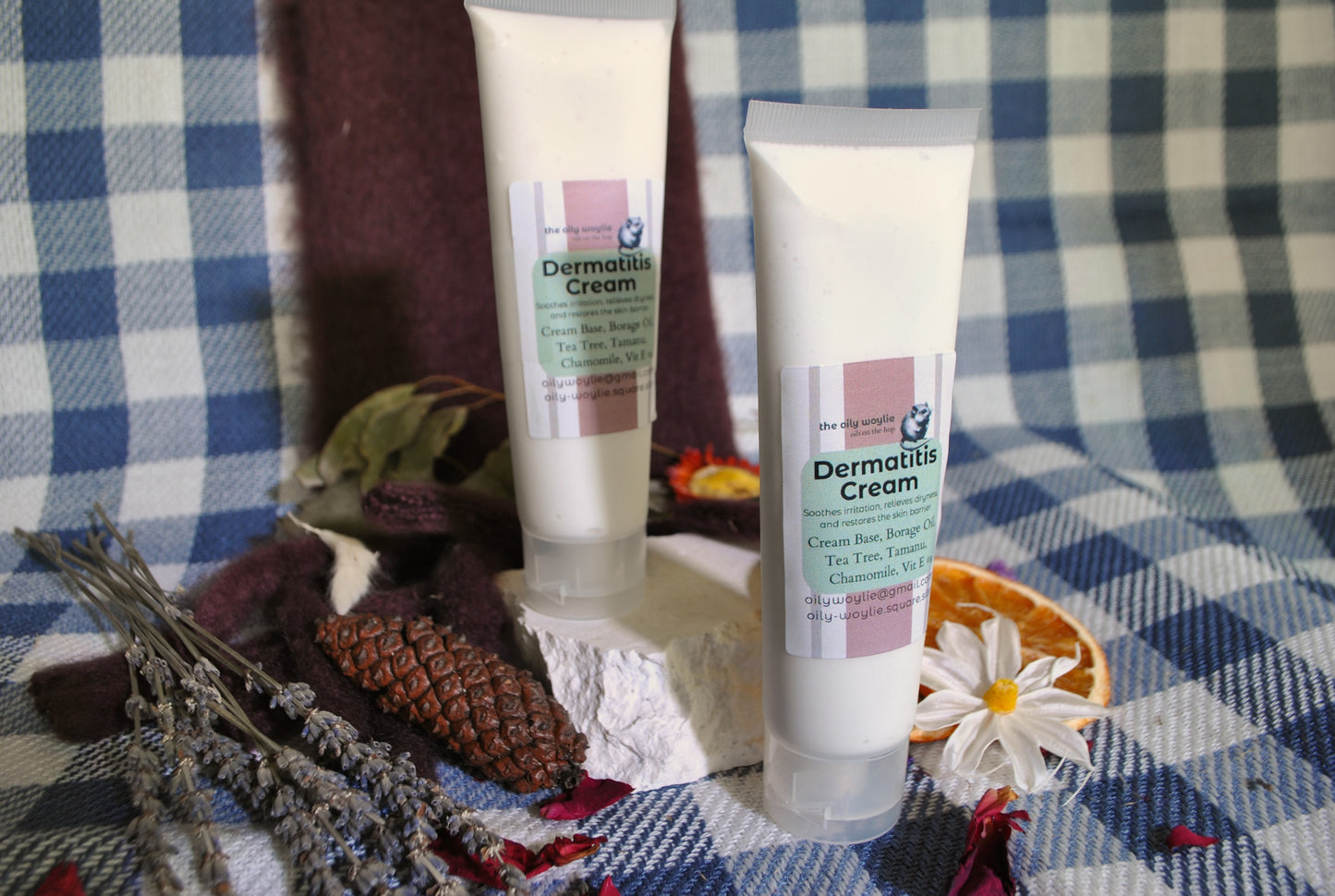 Two tubes of Dermatitis Cream on a checkered fabric background with dried flowers and leaves.