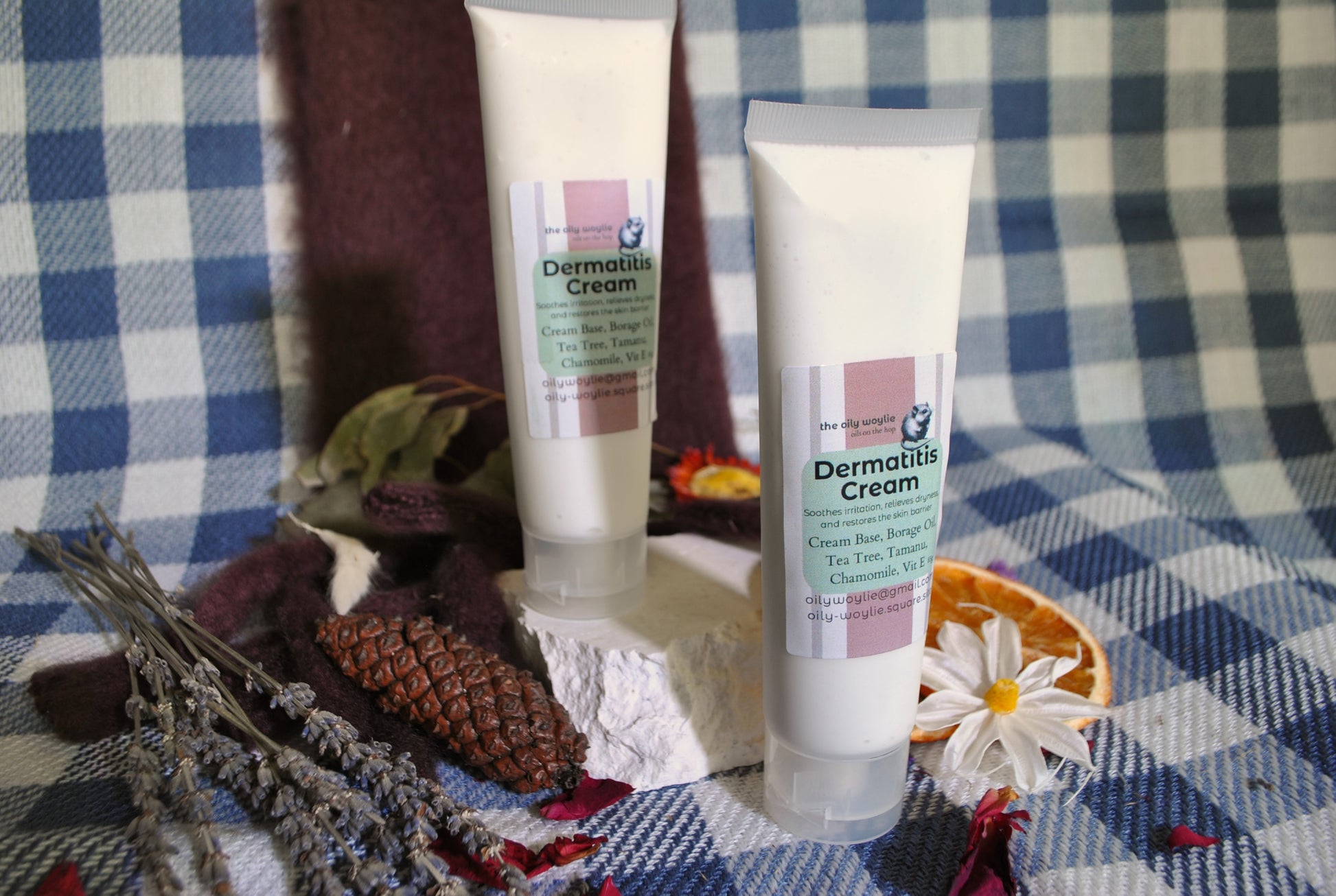Two tubes of Dermatitis Cream on a checkered fabric background with dried flowers and leaves.