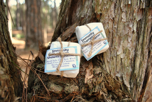 Two shower steamers labeled 'Immunity' hanging from a tree branch in a forest setting.