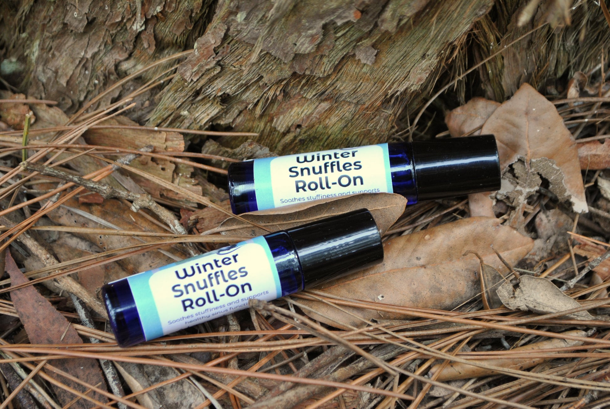 Two 'Winter Shuffles Roll-On' bottles on dry leaves and twigs.