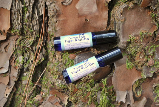 Two bottles of 'Tame the Tiger Roll-On' on a natural background with tree bark and moss.