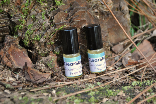Two ClearSkin coconut oil fragrances bottles on a natural background with leaves and wood.