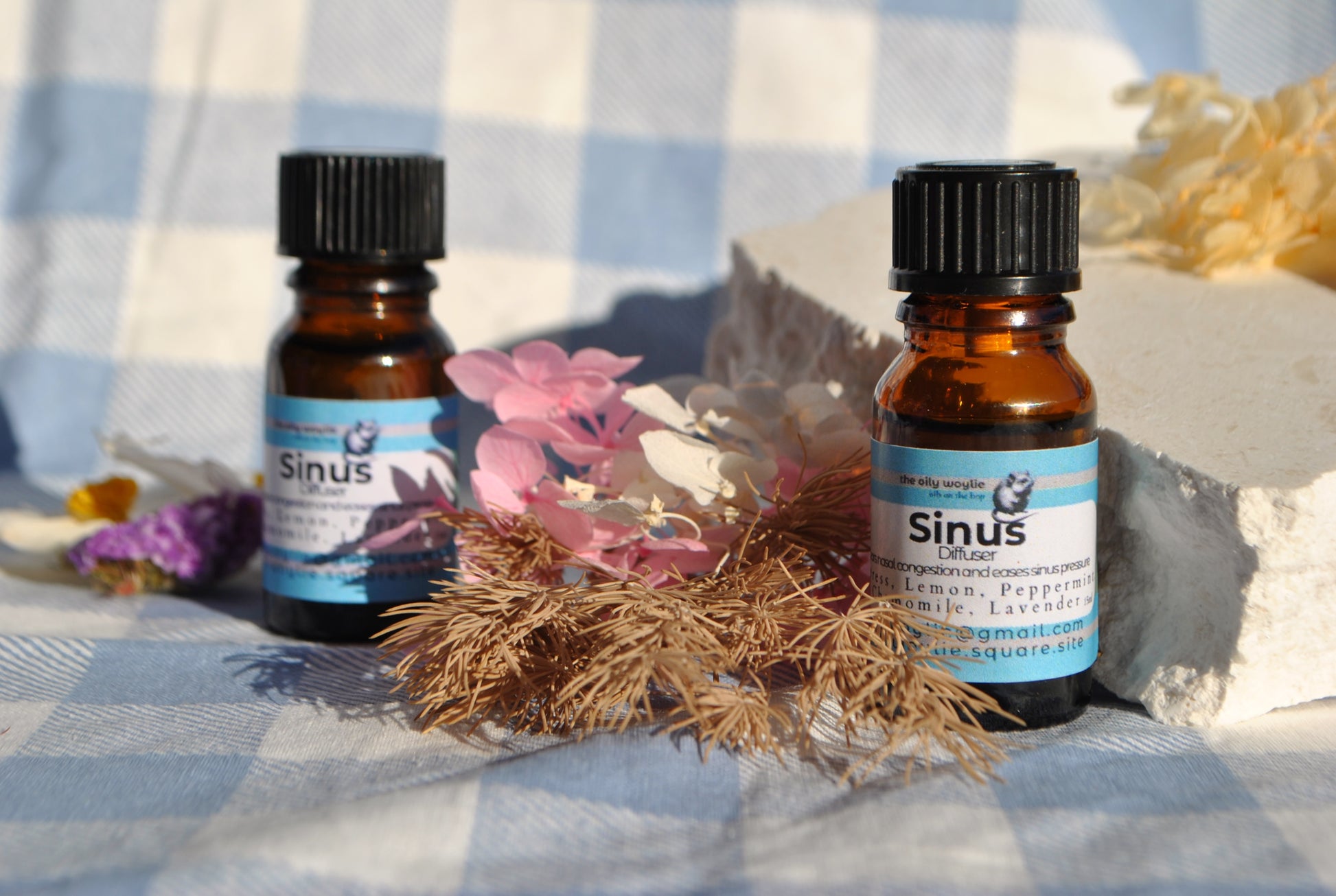 Two bottles of 'Sinus' essential oil on a checkered fabric background with flowers and herbs.