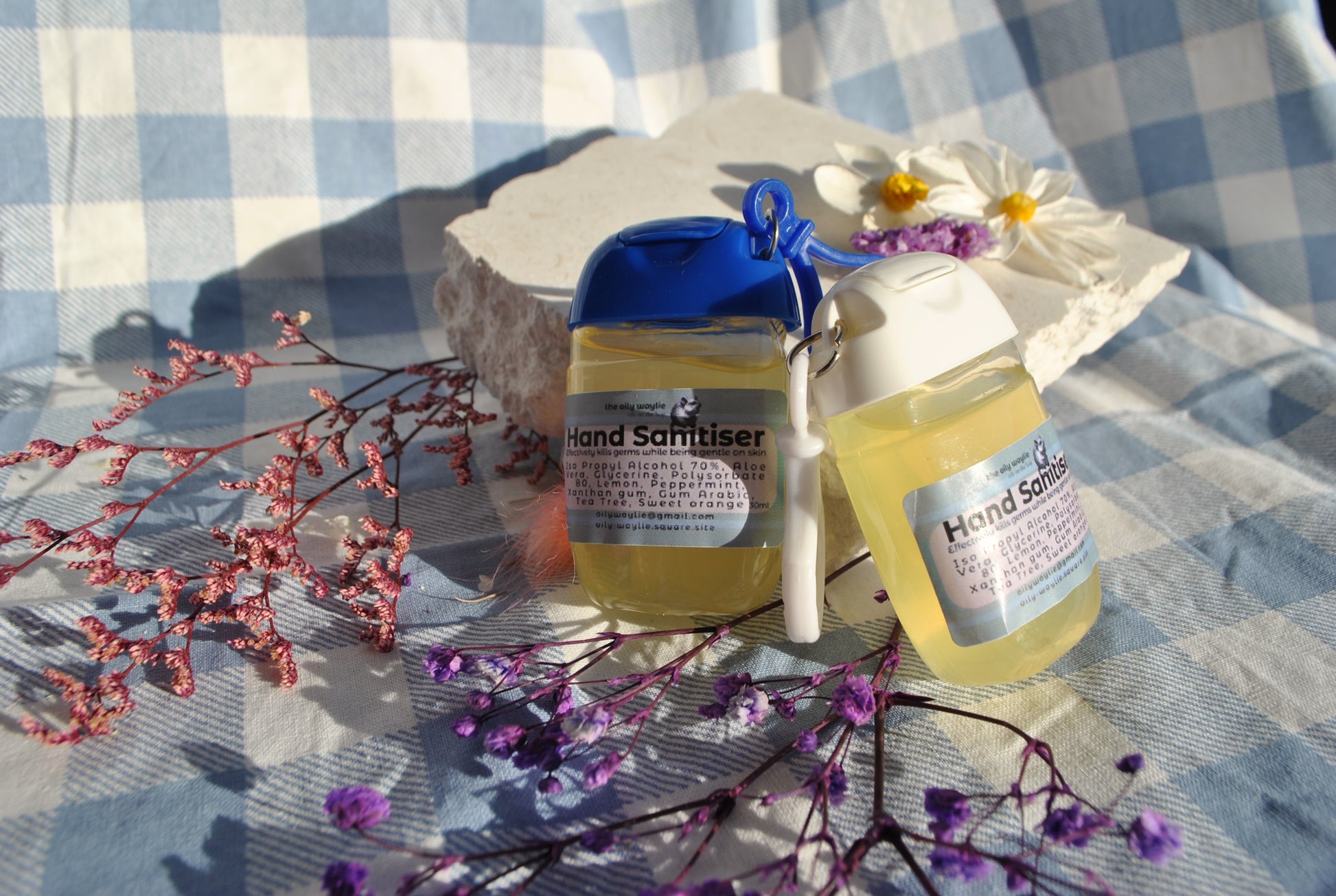 Two bottles of hand sanitizer on a checkered tablecloth with flowers and branches.