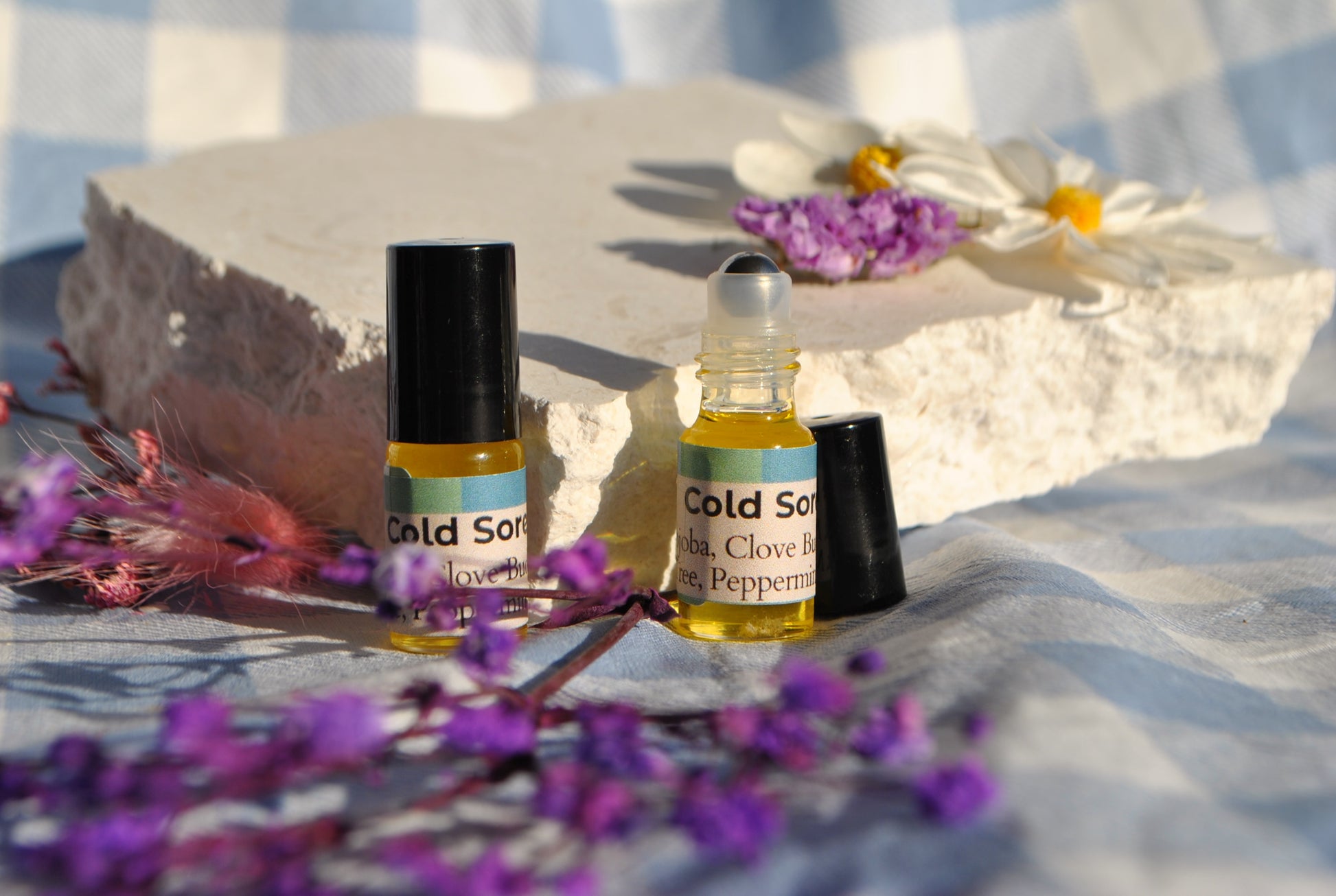 Two small bottles of 'Cold Soothe' on a textured surface with flowers and a stone in the background.