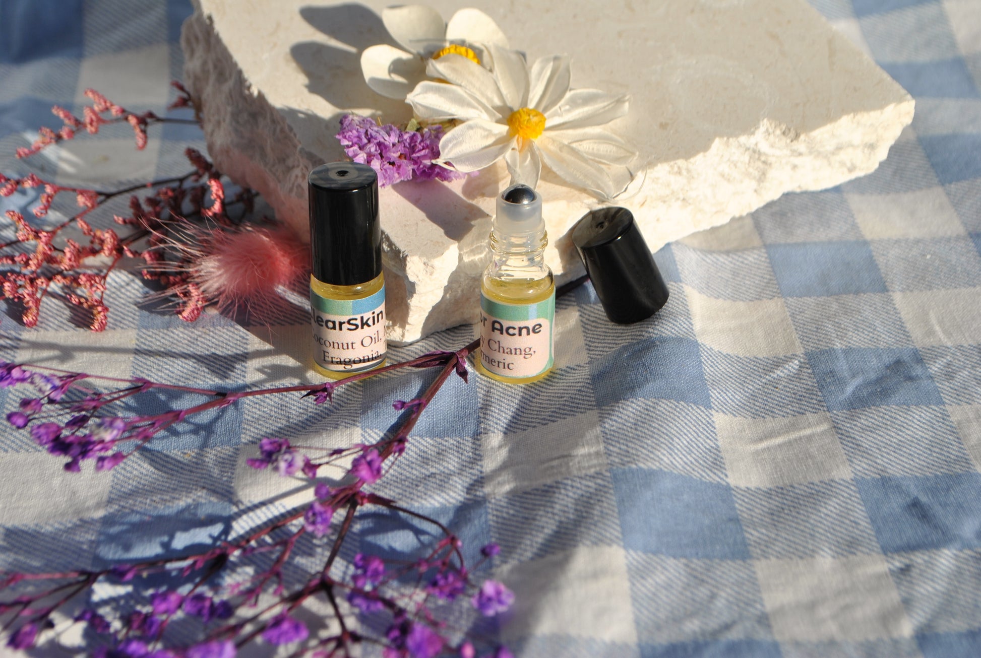 Two small bottles of skincare products on a checkered fabric background with flowers and feathers.