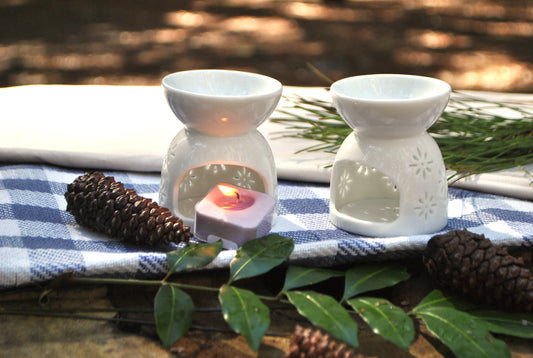Two white wax warmers with lit candles on a blue checkered cloth outdoors.