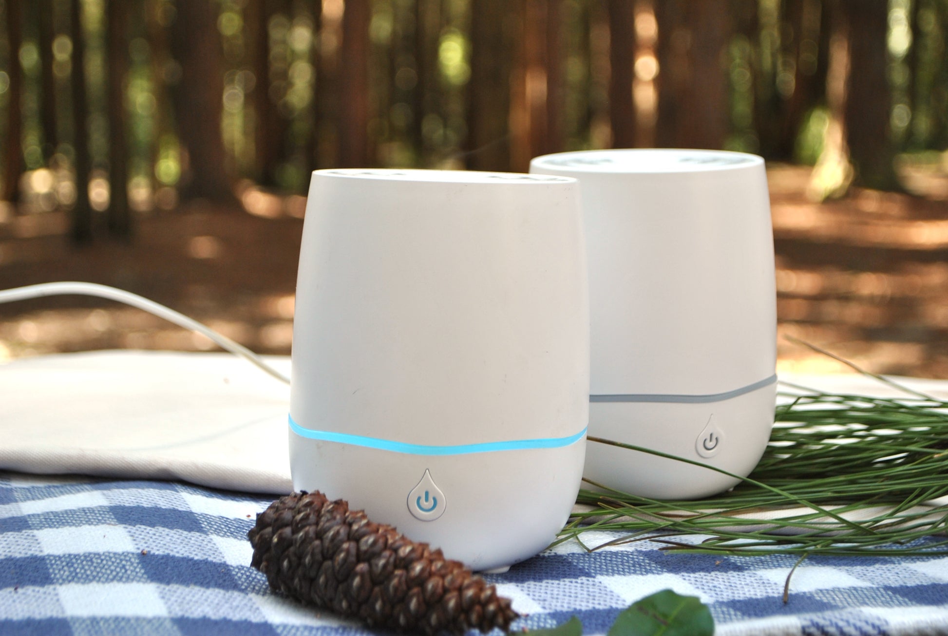 Two white humidifiers with blue lights on a table outdoors, surrounded by nature.