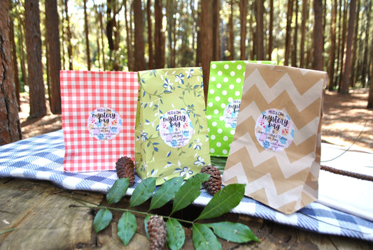 Four gift bags with labels on a wooden surface in a forest setting