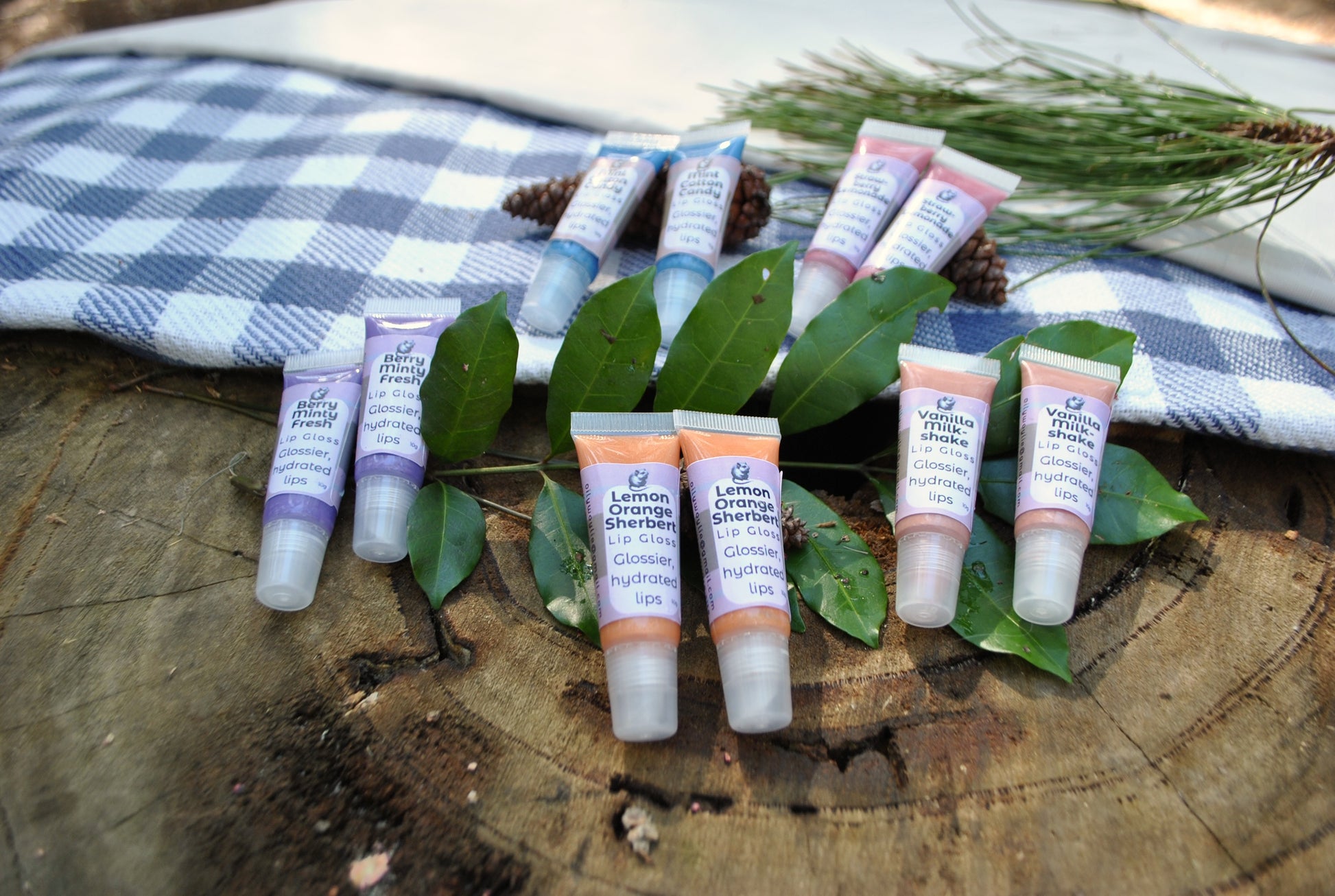 Lip gloss tubes on green leaves with a checkered cloth in the background