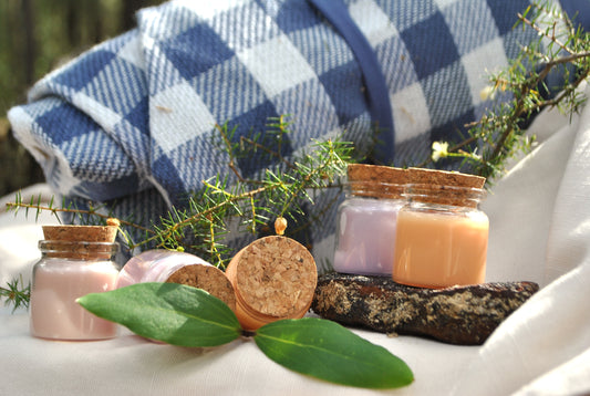 Small jars with cork lids on a stone surface with greenery and a checkered cloth in the background