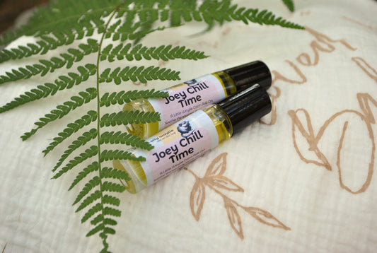 Two 'Joey Chill Time' rollerball products on a textured surface with fern leaves.