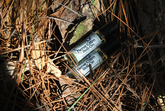 Two bottles of 'Nerve Calm Roll-On' lying on dry leaves and twigs.