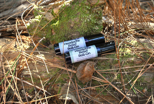 Two bottles of Headache Roll-On on a forest floor with moss and leaves.