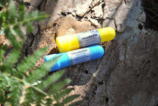 Two headache sticks, one blue and one yellow, on a textured surface with greenery.