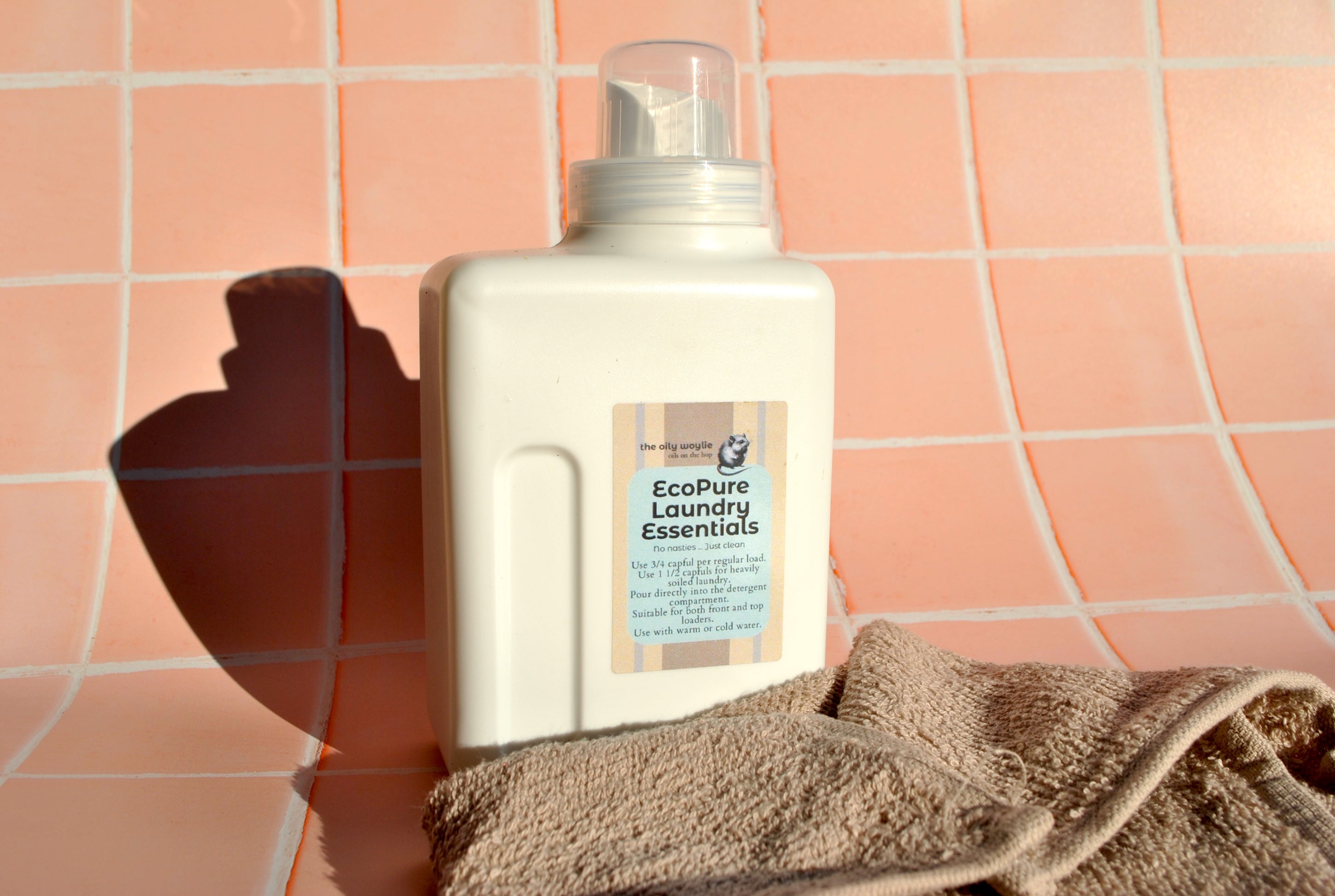 EcoPure Laundry Essentials bottle on a towel against a tiled wall background