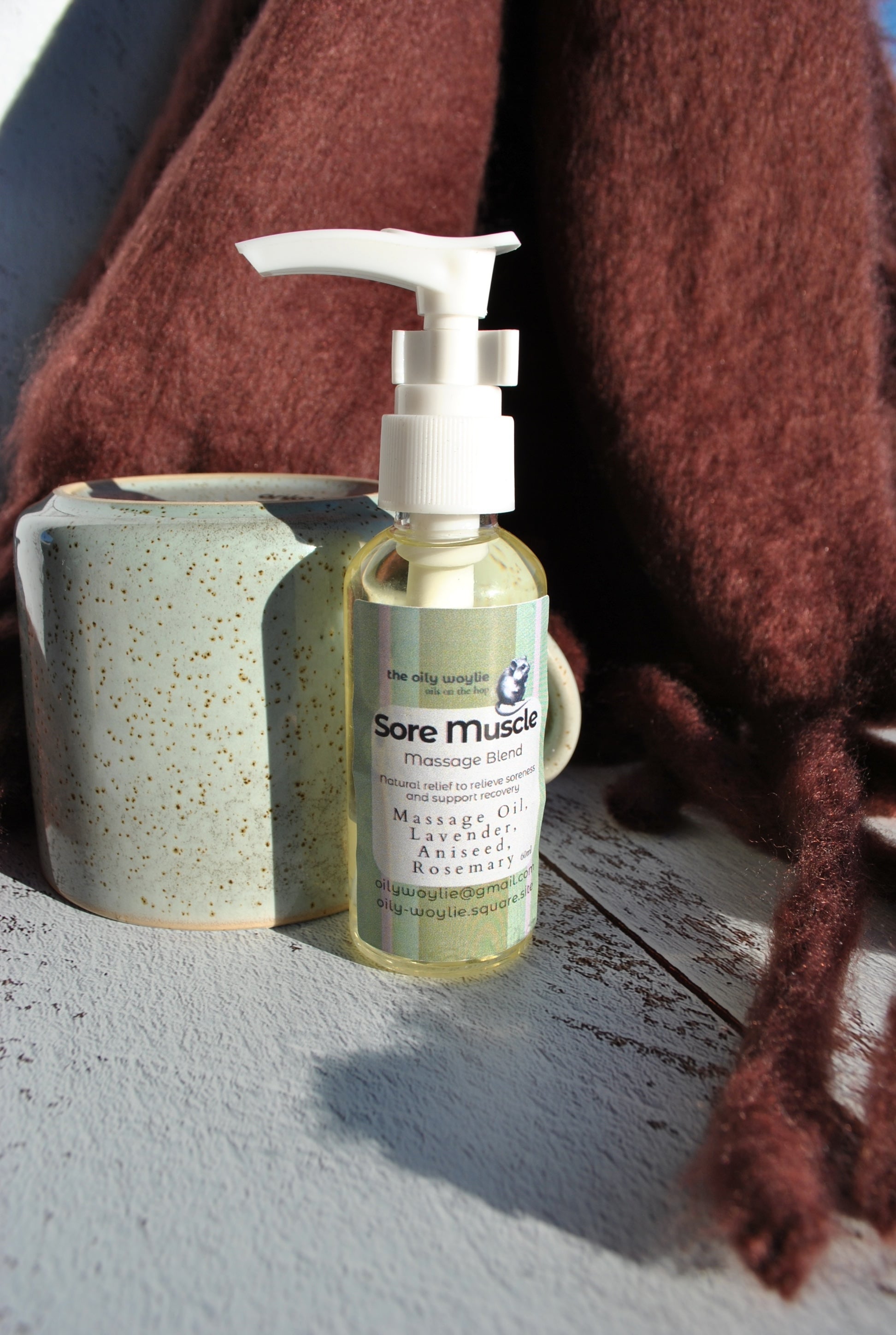 Bottle of 'Sore Muscle' massage oil with a ceramic container on a textured surface.