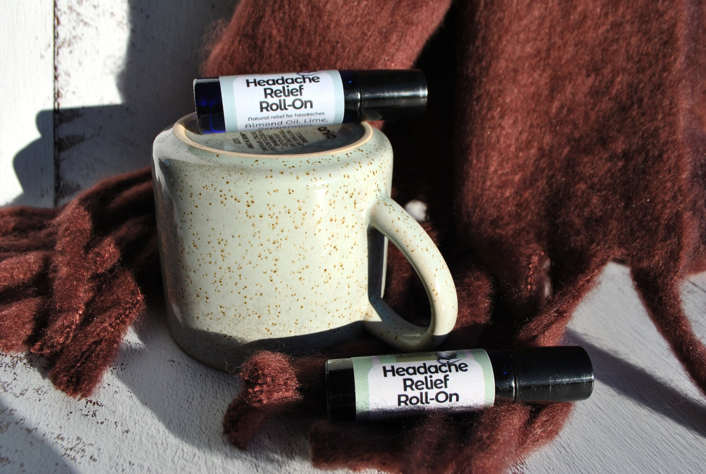 Two headache relief roll-ons on a mug with a brown scarf in the background