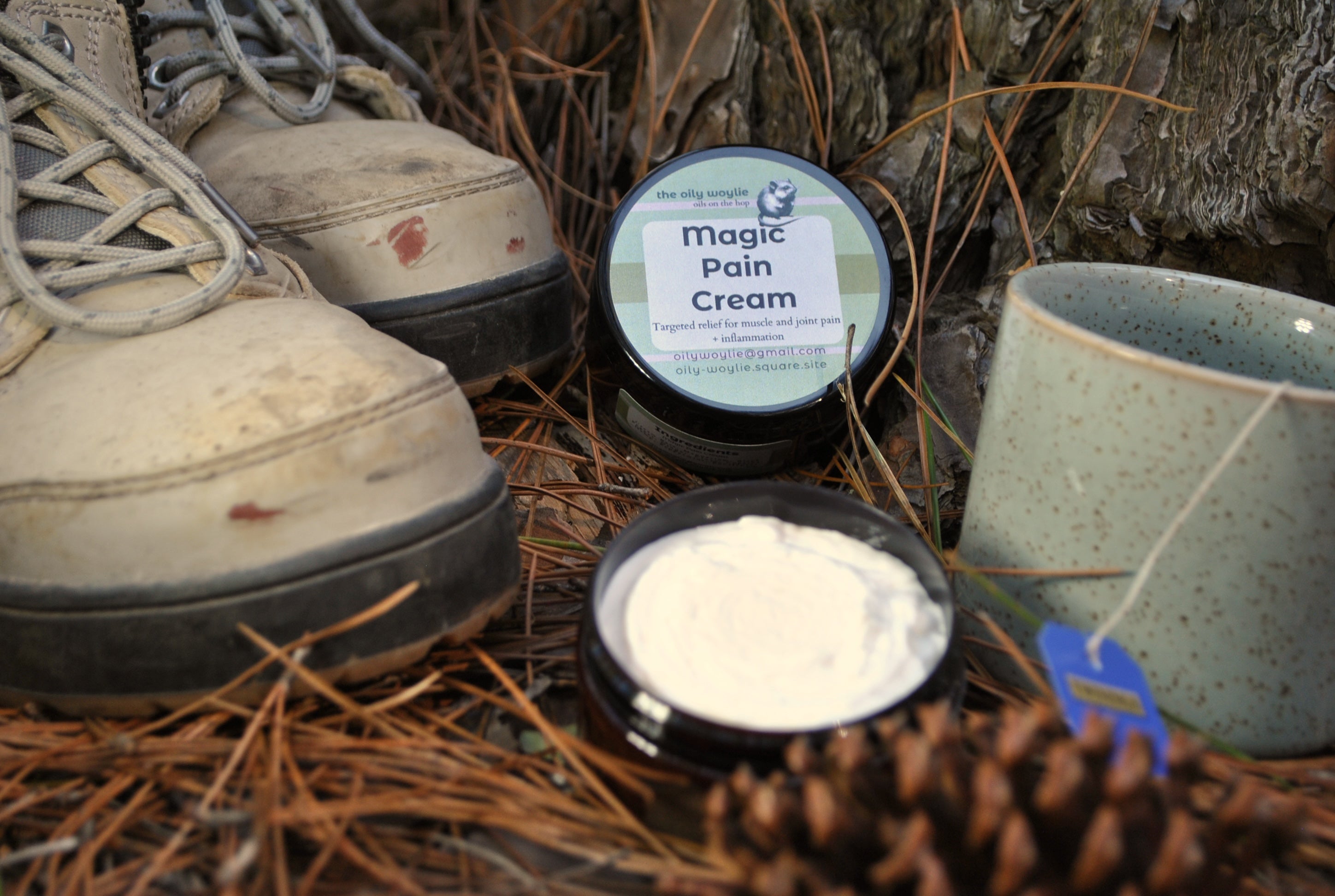 Two containers of 'Magic Pain Cream' on a natural background with hiking boots and a pot.