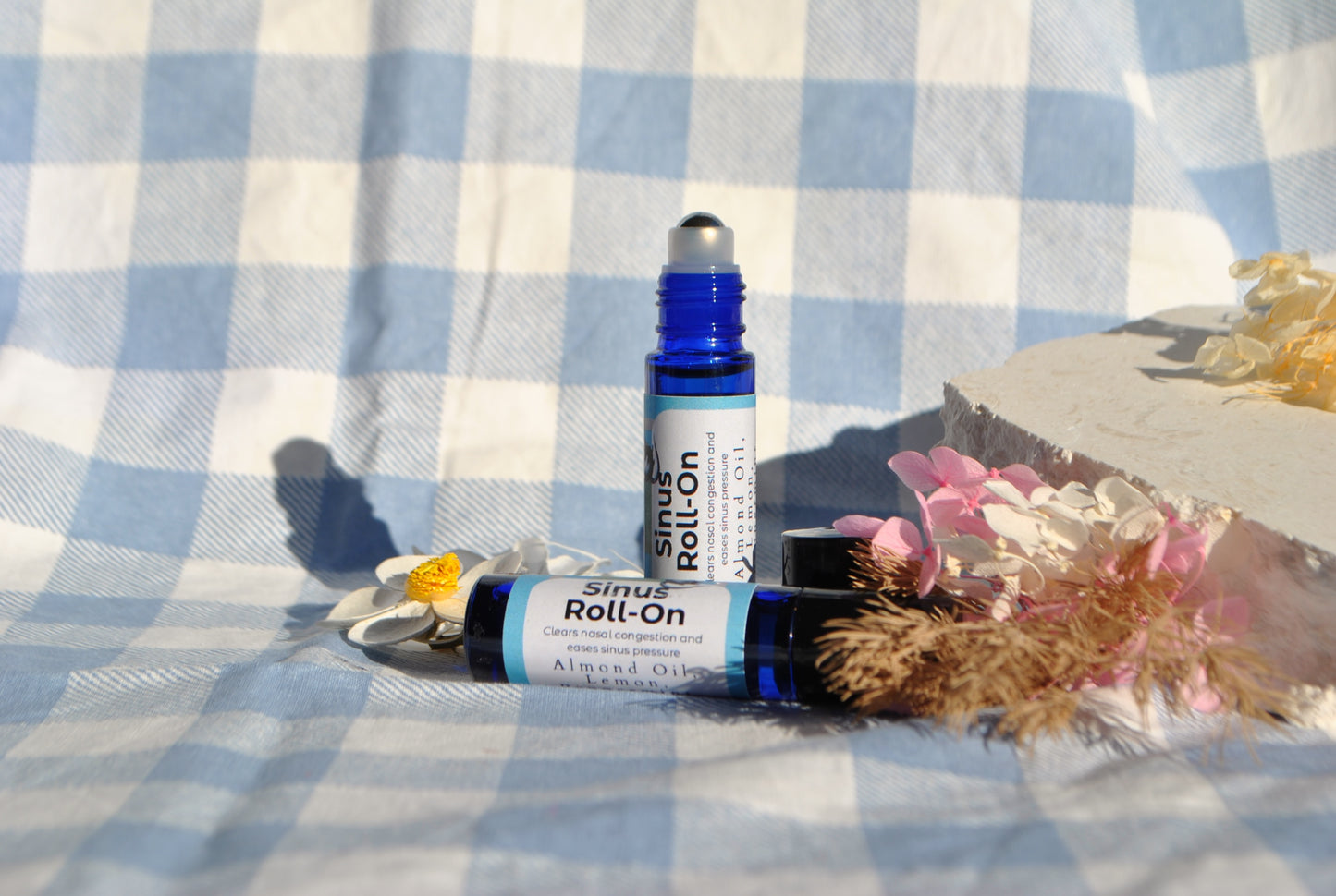 Sinus Roll essential oil roller blend, natural support for sinus relief on a checkered fabric background with flowers.
