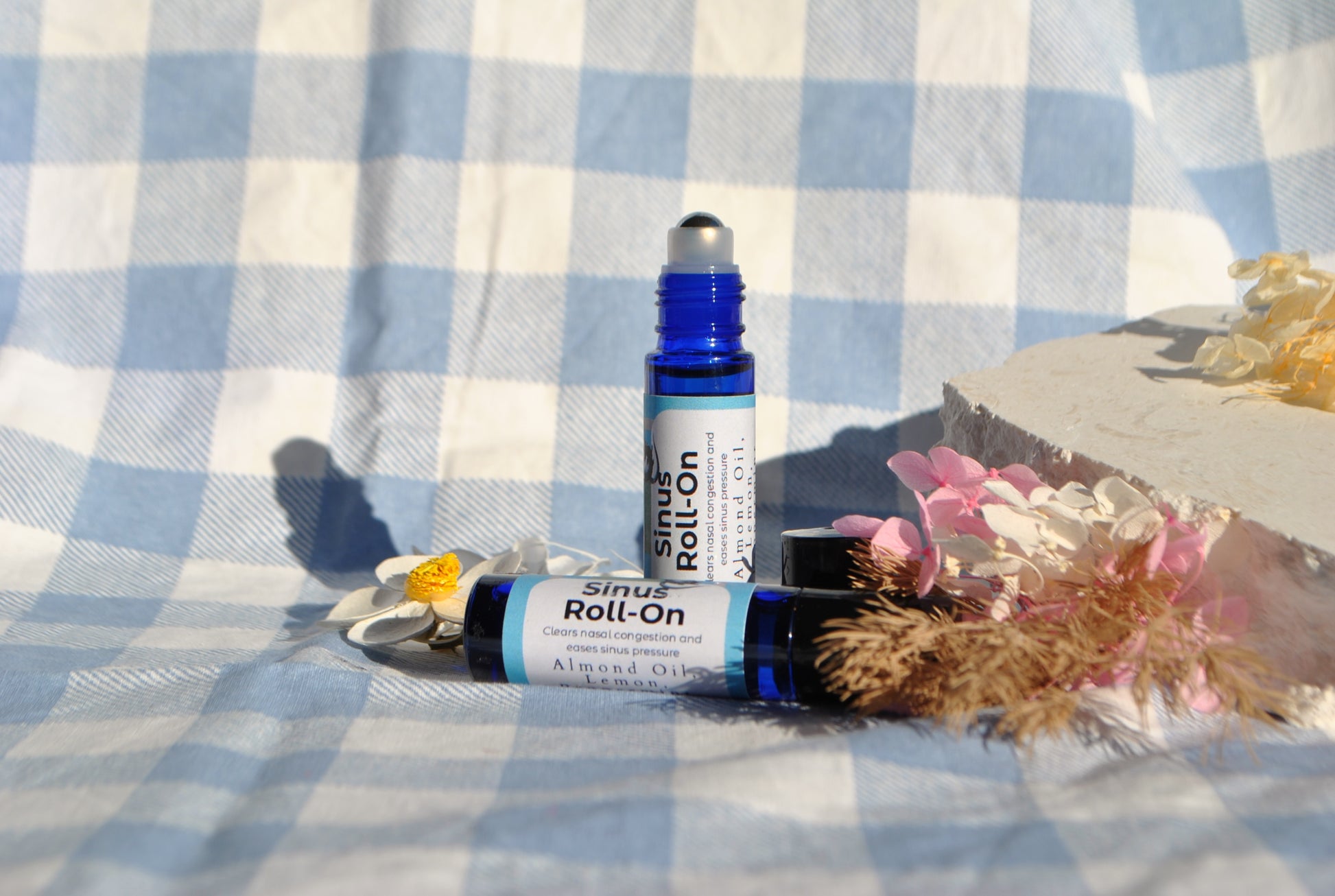 Sinus Roll essential oil roller blend, natural support for sinus relief on a checkered fabric background with flowers.