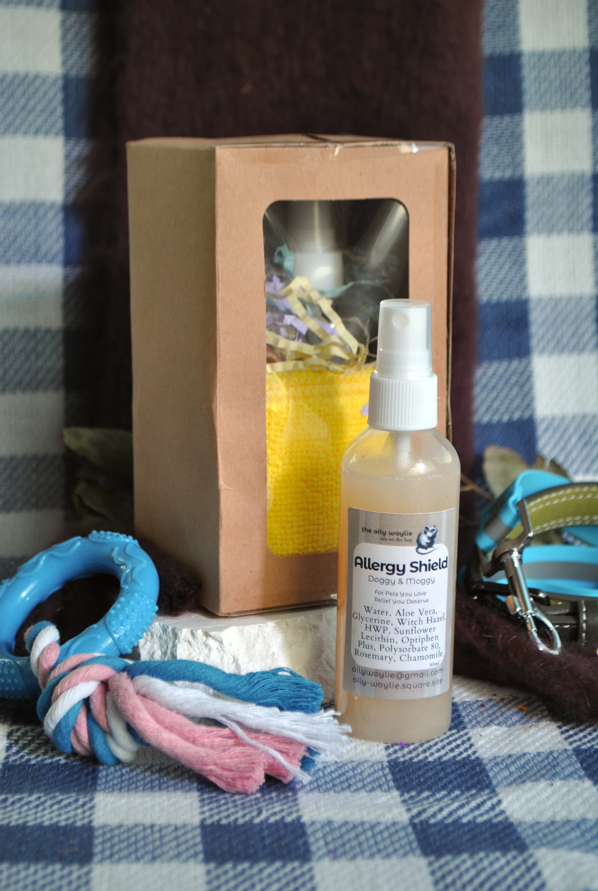 Allergy Shield spray bottle, natural spray to support pet parents with allergies to pet fur on a checkered fabric background with a dog toy and packaging.