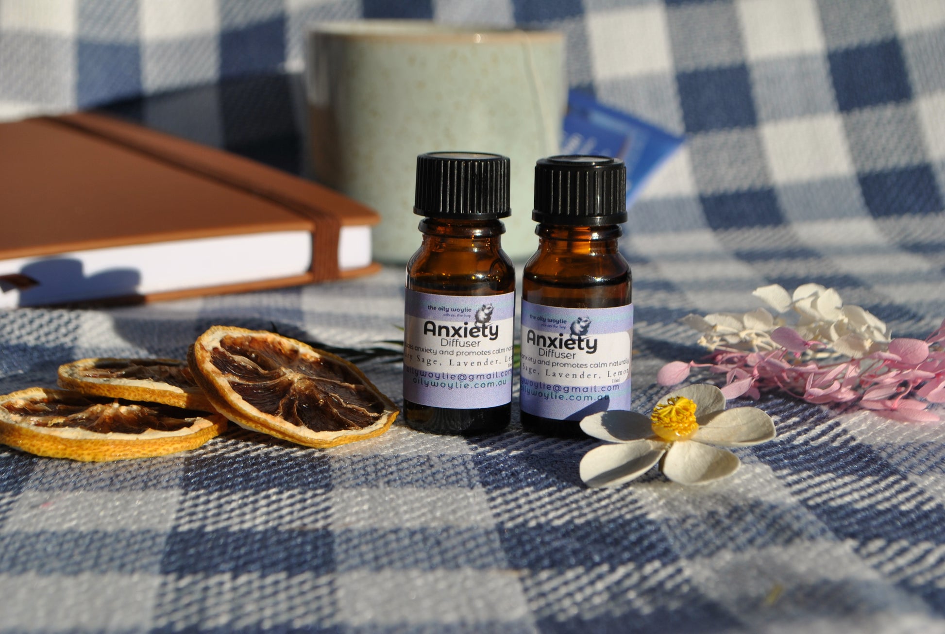 Anxiety Diffuser essential oil blend bottle, natural support for calm and relaxation on a checkered tablecloth with dried oranges and flowers.