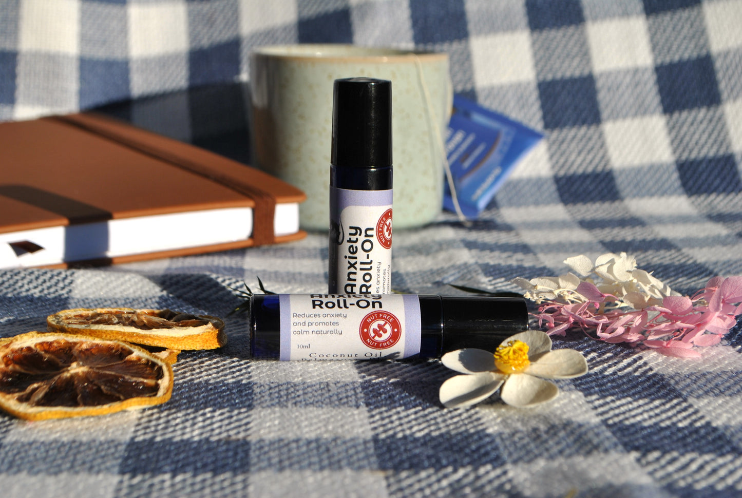Anxiety Roll essential oil roller blend, natural calming support for stress and anxiety Two roll-on bottles on a checkered tablecloth with books and flowers.