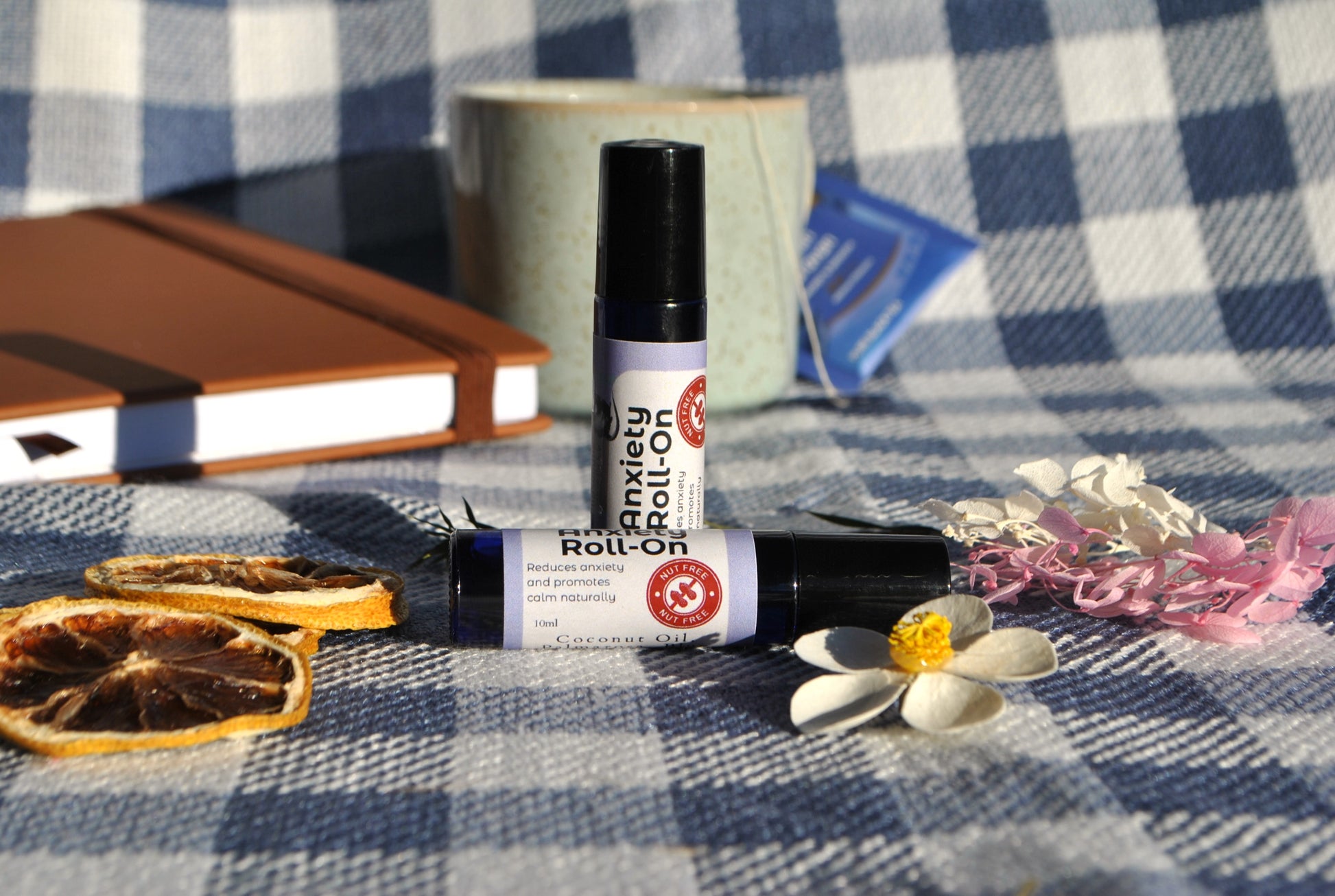 Anxiety Roll essential oil roller blend, natural calming support for stress and anxiety Two roll-on bottles on a checkered tablecloth with books and flowers.