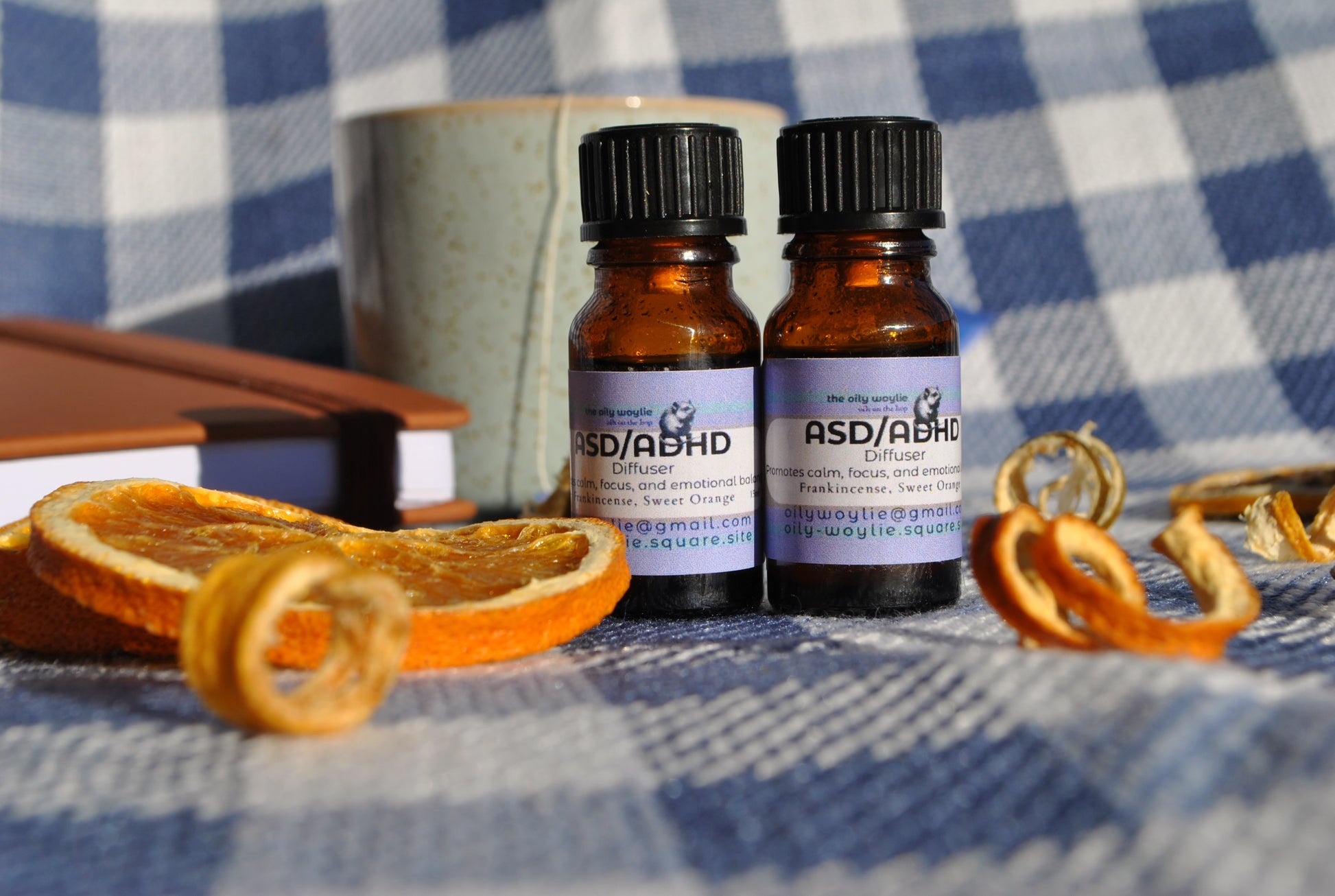 ASD/ADHD Diffuser essential oil blend bottle, calming support for focus and relaxation on a checkered fabric background with dried oranges.