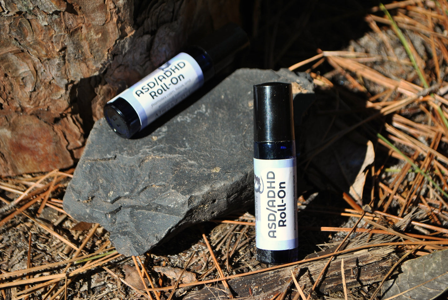 ASD/ADHD Roll essential oil blend in roller bottle, natural calming support on a stone surface with pine needles and leaves.
