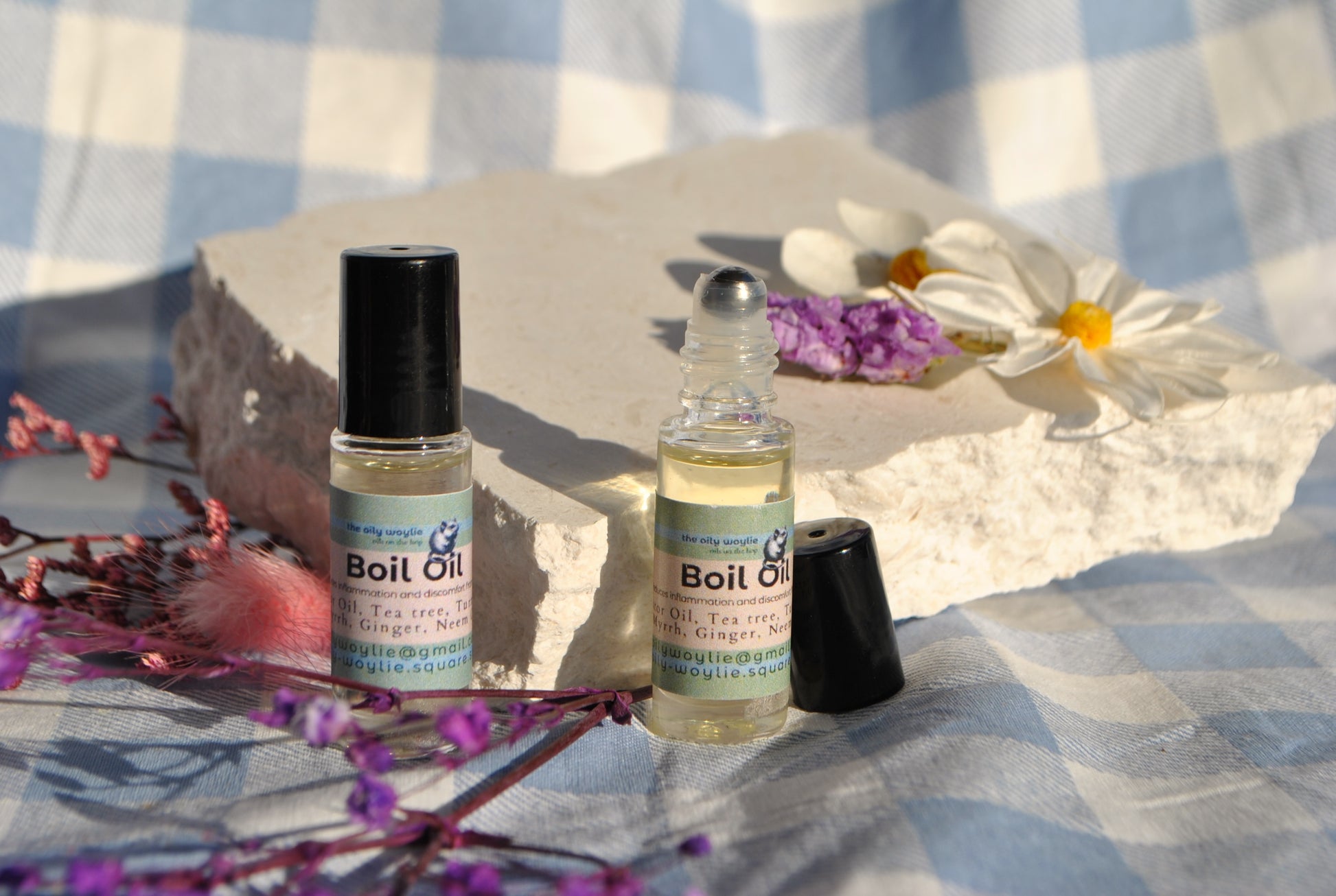 Boil Oil essential oil blend bottle, natural topical support for skin irritation on a checkered fabric background with flowers.