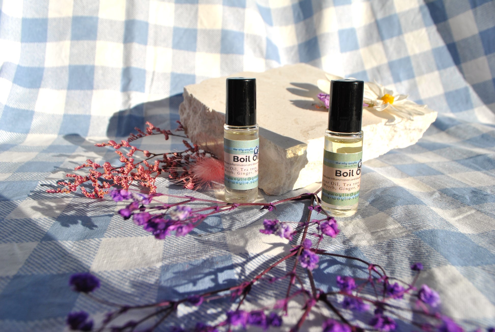 Boil Oil essential oil blend bottle, natural topical support for skin irritation on a checkered fabric background with purple flowers.