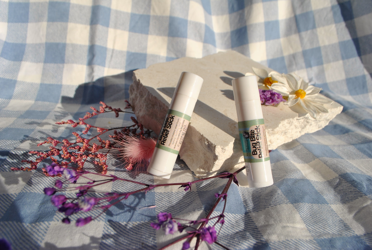 Bug Bite Relief Stick tube, natural soothing balm for insect bites on a stone with flowers and a checkered fabric background