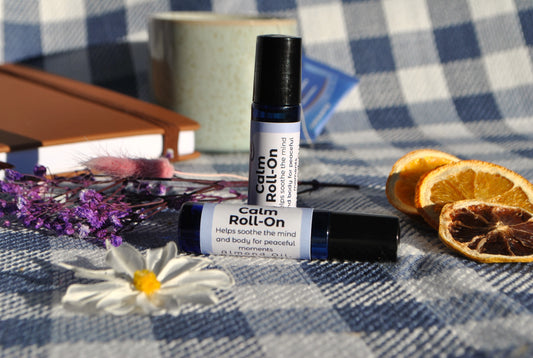 Calm Roll essential oil roller blend, promotes relaxation and stress relief on a checkered tablecloth with flowers and oranges