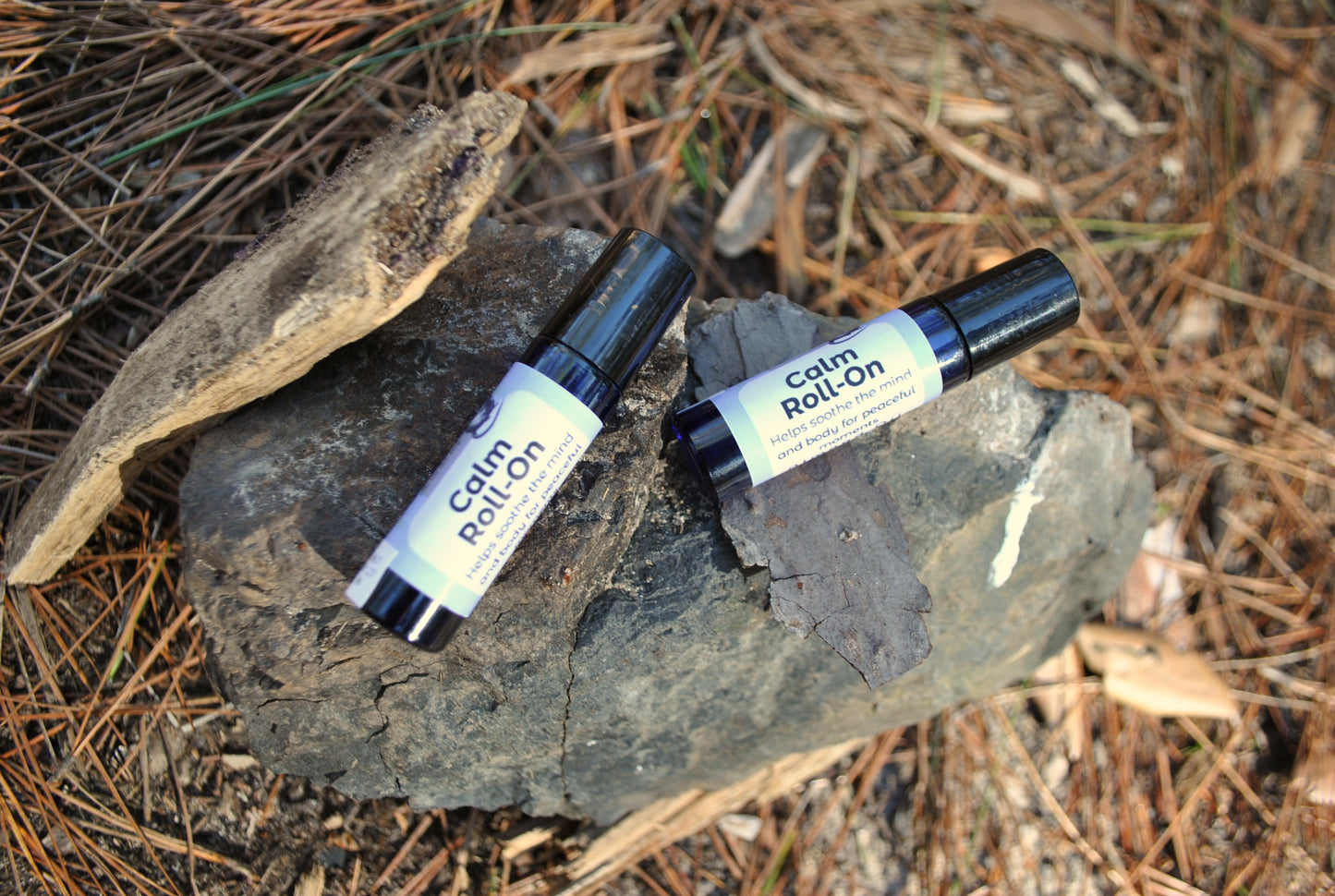 Calm Roll essential oil roller blend, promotes relaxation and stress relief on a rock with pine needles in the background