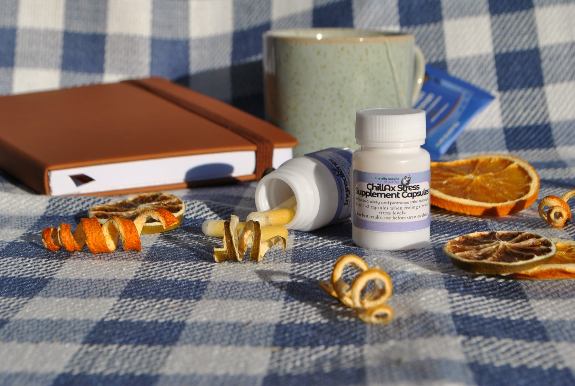 ChillAx Stress Supplement Capsules bottle, natural supplement to support relaxation and stress relief on a checkered tablecloth with dried oranges and a notebook.