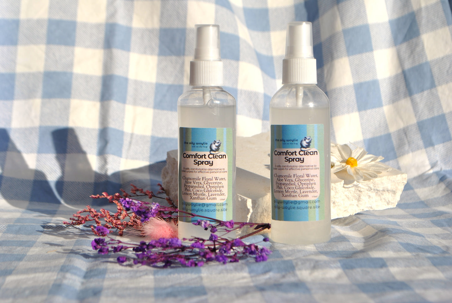 Comfort Clean Spray bottle, natural toilet spray to use instead of wet wipes on a checkered fabric background with flowers and a daisy.