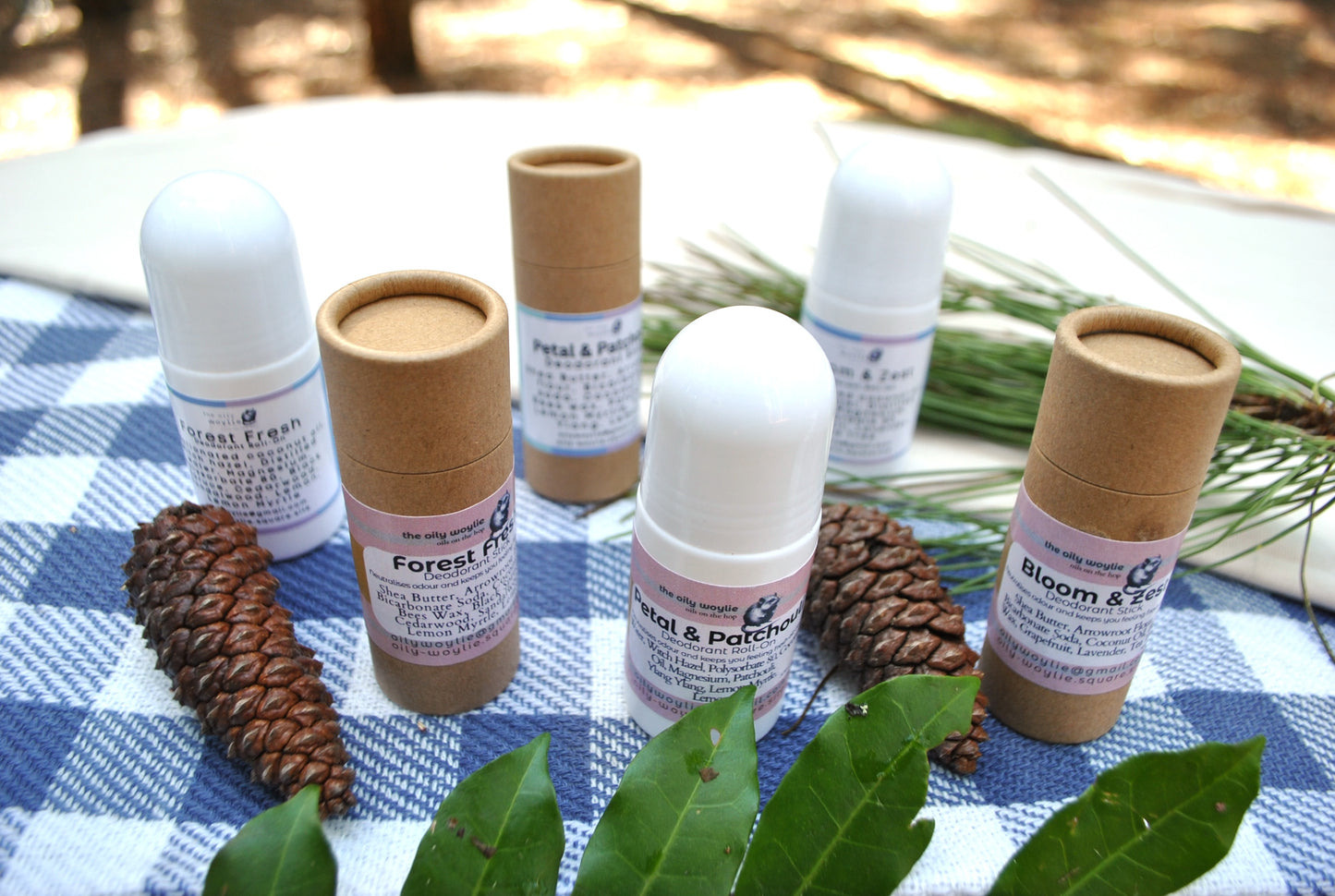 Natural deodorant family collection – Roll-On and Stick deodorants in Bloom & Zest, Forest Fresh, and Petal & Patchouli scents on a checkered cloth with greenery