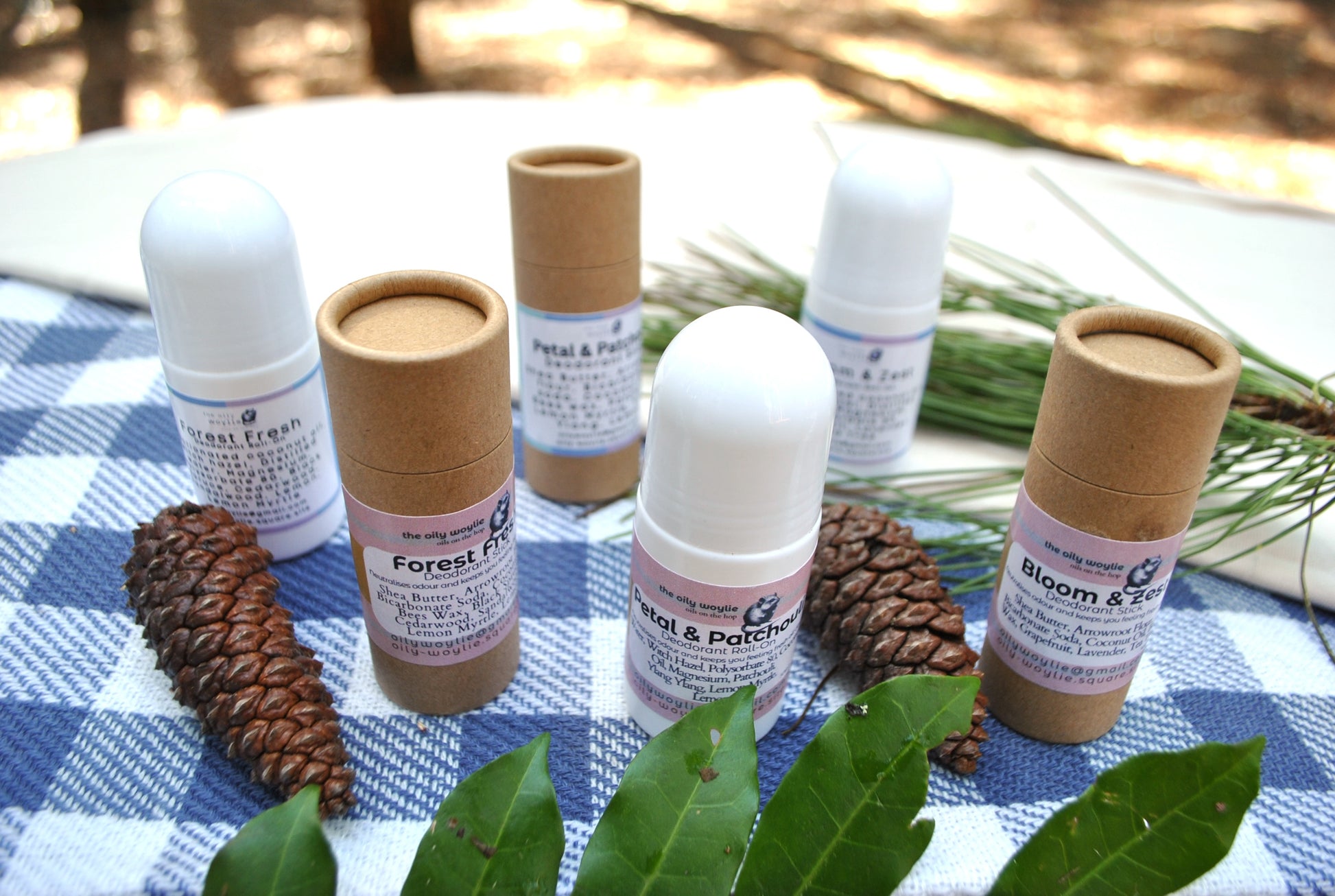 Natural deodorant family collection – Roll-On and Stick deodorants in Bloom & Zest, Forest Fresh, and Petal & Patchouli scents on a checkered cloth with greenery