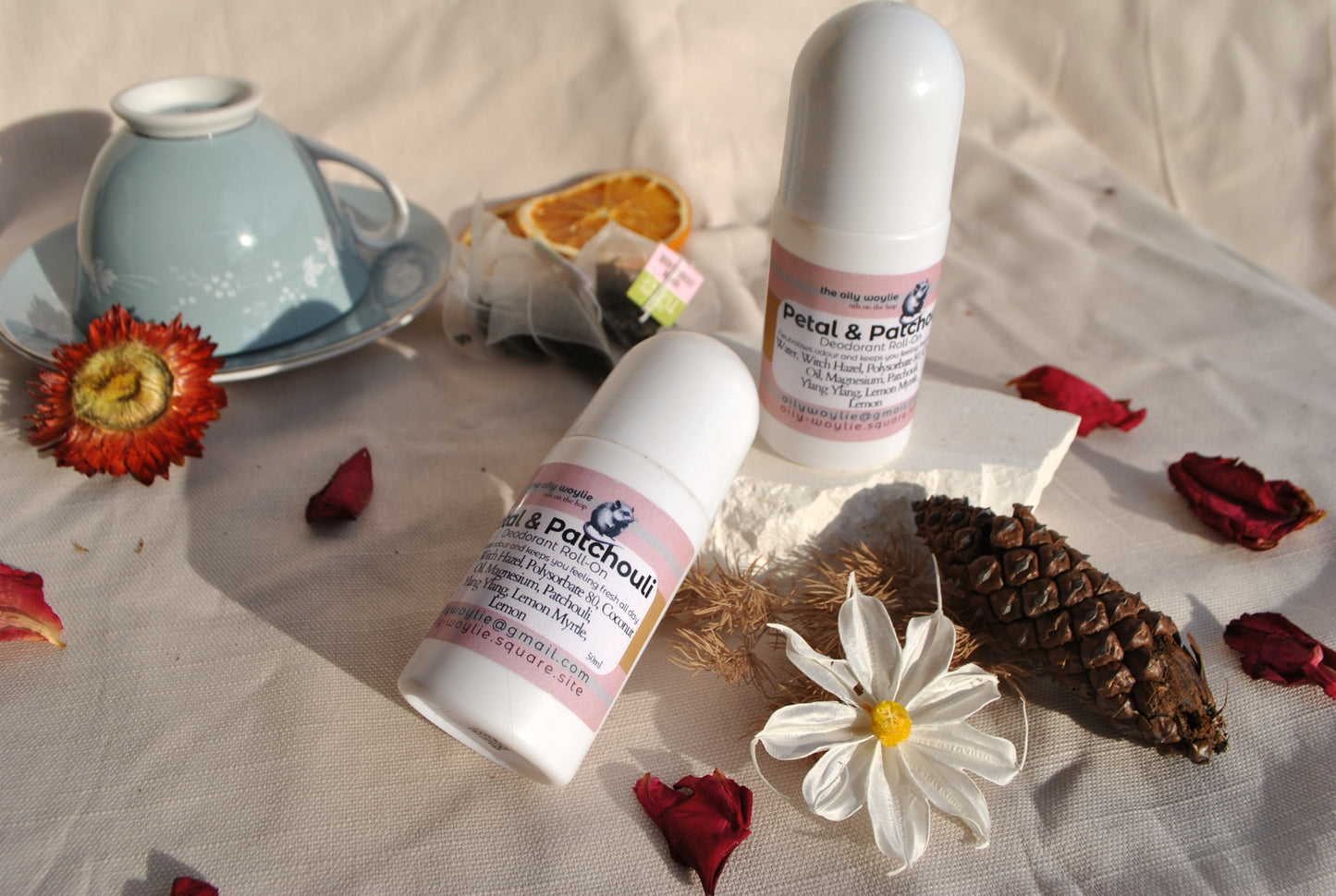 Deodorant Roll-On Petal & Patchouli bottle, natural floral deodorant on a textured surface with flowers and a teacup.