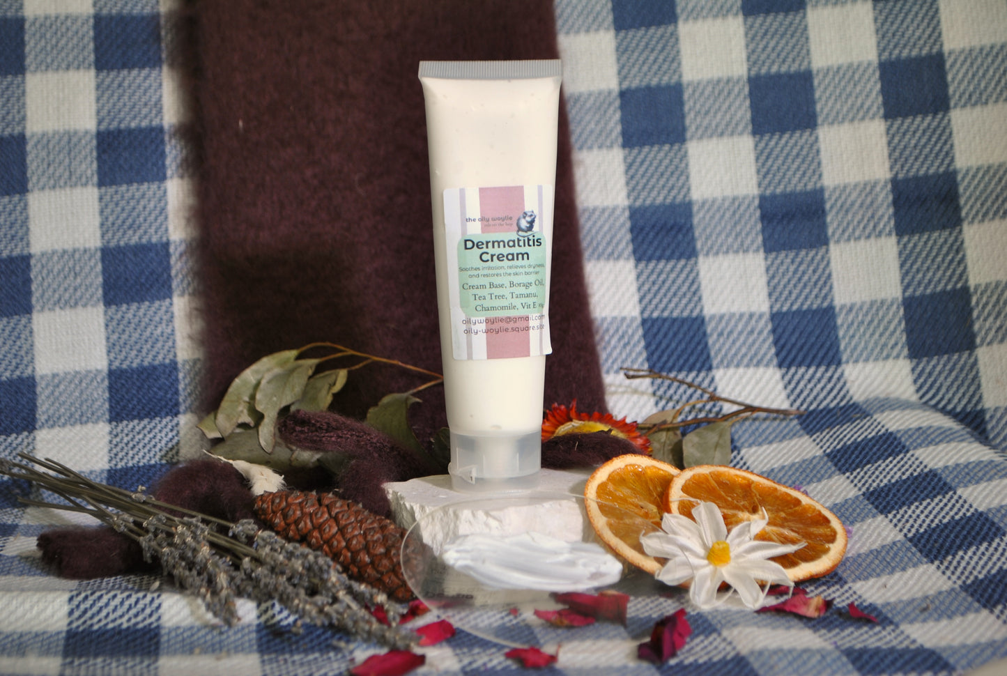 Dermatitis Cream tube, natural cream to soothe irritated and sensitive skin on a checkered fabric background with dried oranges and flowers.