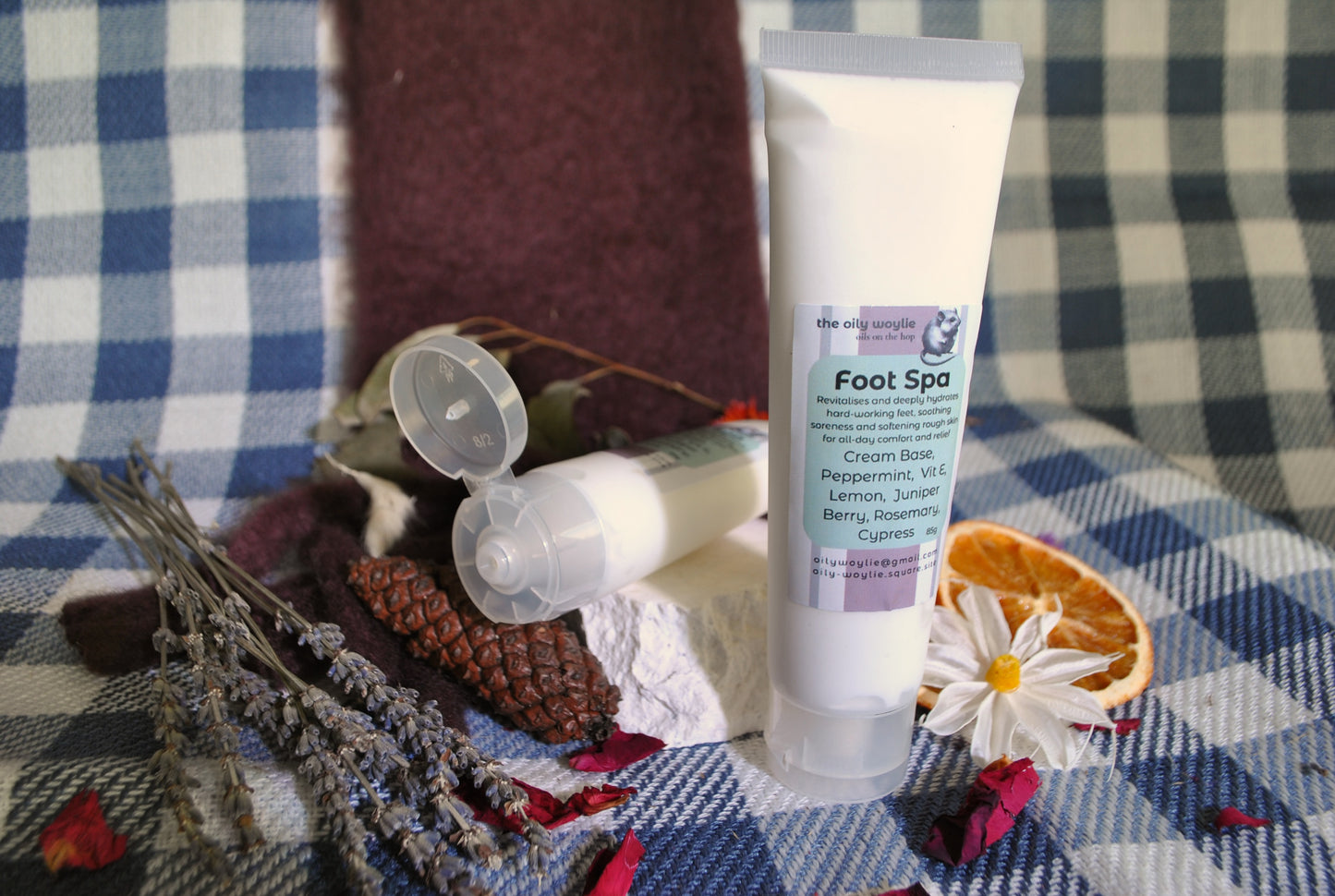 Foot Spa cream tube, natural foot rub with essential oils for relaxation and soft feet on a checkered fabric background with dried flowers and herbs.