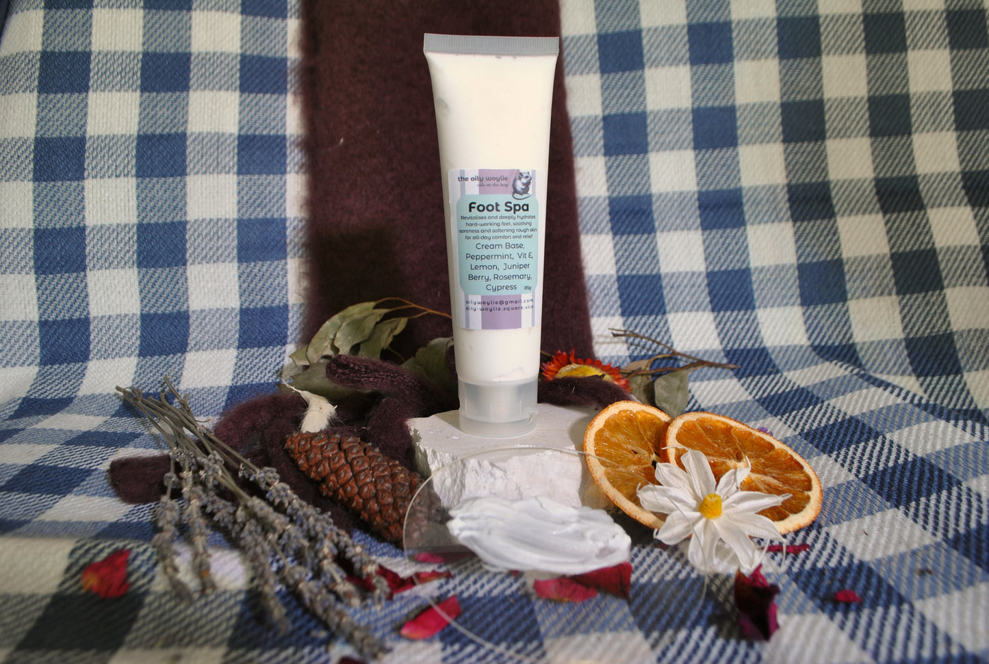Foot Spa cream tube, natural foot rub with essential oils for relaxation and soft feet with dried oranges, flowers, and leaves on a checkered fabric background