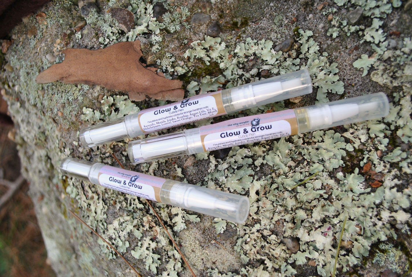 Glow & Grow Cuticle Pen, natural cuticle and nail oil treatment on a textured surface with green and brown tones.