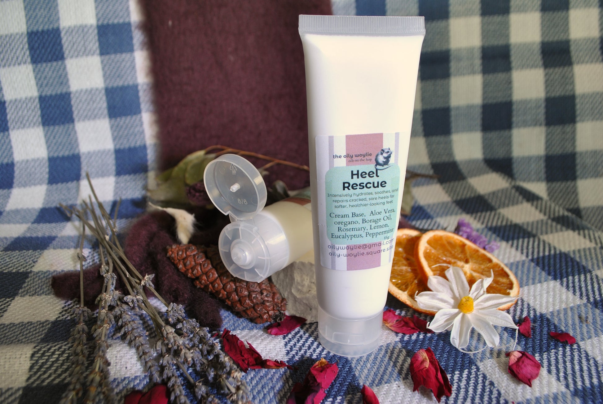 Heel Rescue cream tube, natural foot cream for cracked heels and dry feet on a checkered fabric background with dried flowers and herbs.