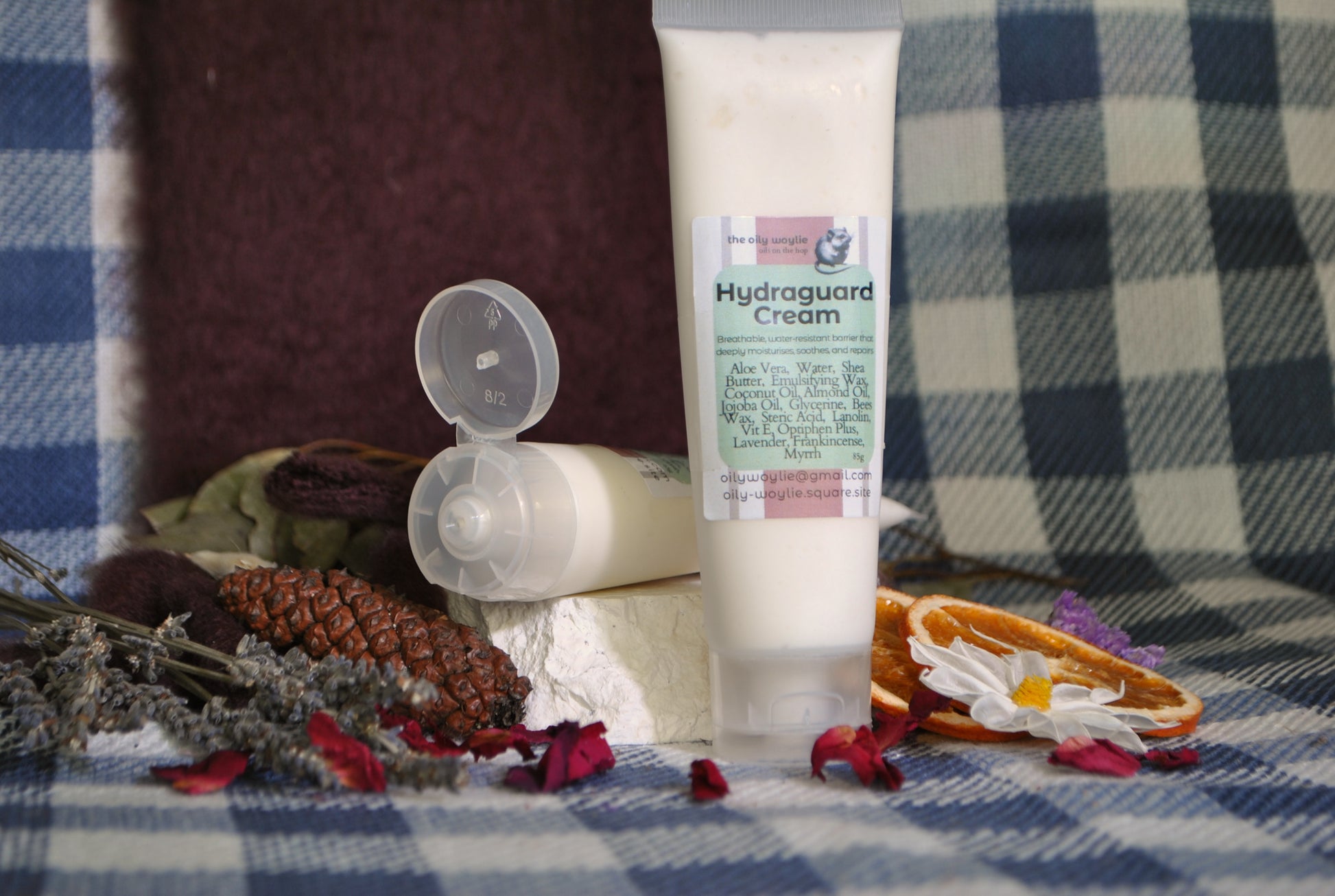 Hydraguard Cream tube, natural moisturising cream for dry skin protection on a checkered fabric background with flowers and pinecones.